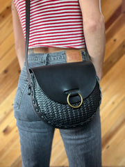 Black stamped leather bag with antique brass oring doorknocker closure worn over the shoulder by tattooed woman