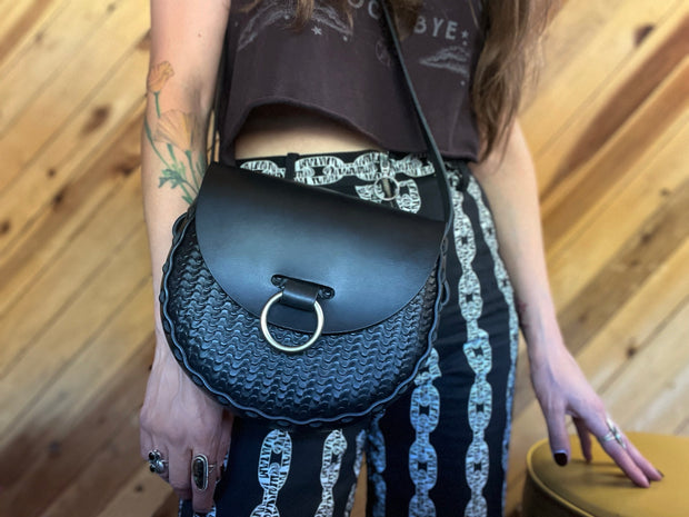 Black stamped leather bag with antique nickel oring doorknocker closure worn over the shoulder by tattooed woman